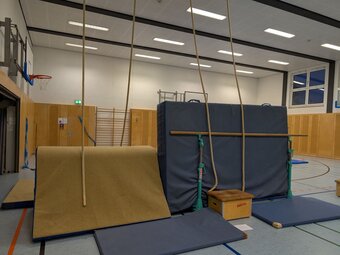 Eine Kletterwand mit heruntergelassenen Tauen an der Hallenwand.