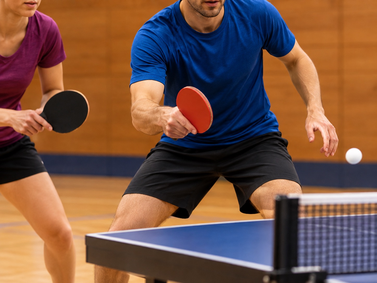 Zwei Personen spielen Tischtennis in einer Sporthalle.
